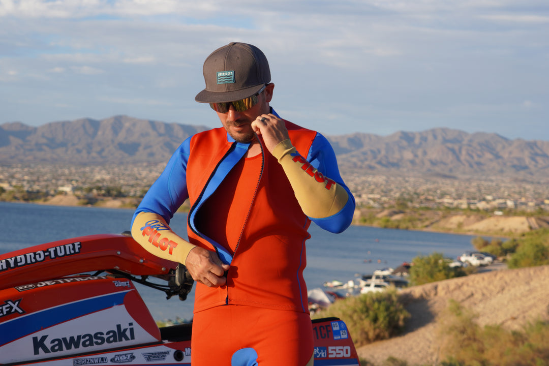 Mark Gomez in the red and blue Vintage Class racing suit standing next to a Kawasaki boat on a scenic background. #color_red-blue
