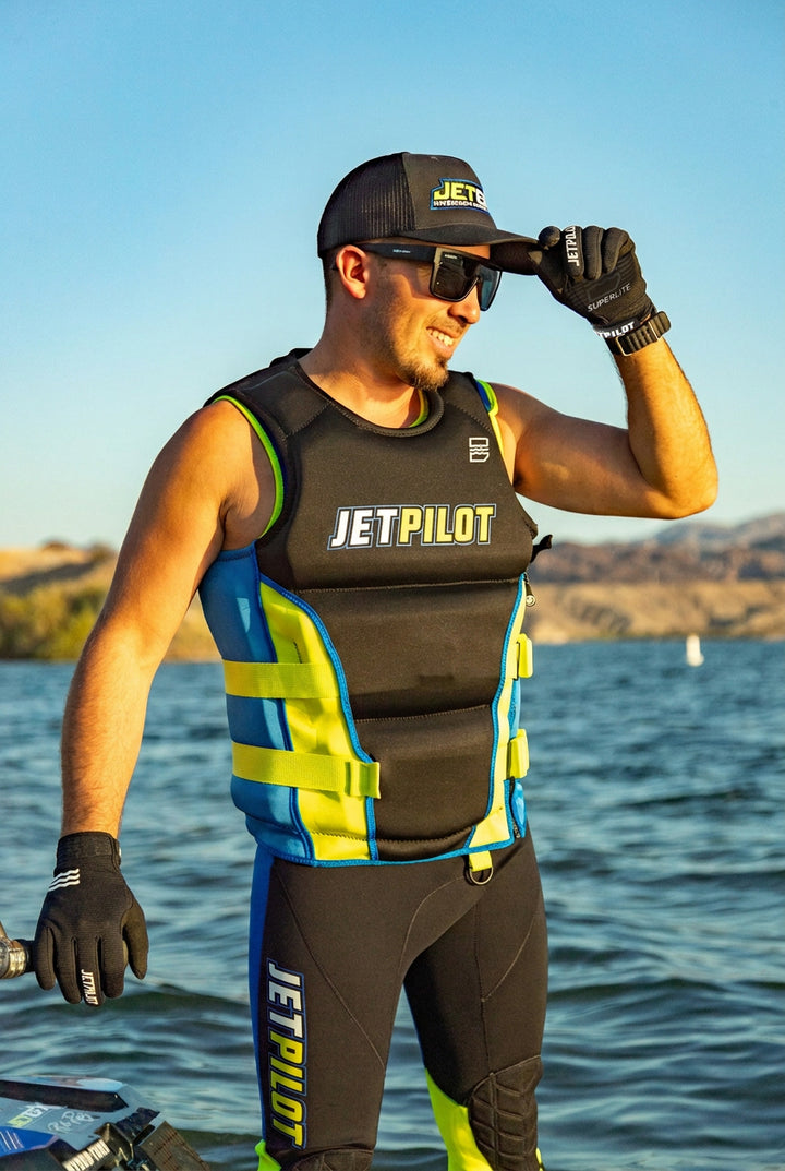 Person wearing JetPilot water sports gear by a body of water with mountains in the background. #color_black