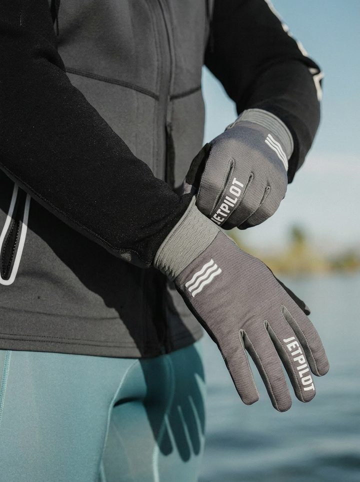 Person wearing gray gloves with 'JETPILOT' branding by a body of water. #color_charcoal
