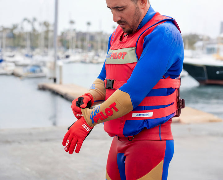 Person wearing a red and blue life jacket and gloves with 'Pilot' branding by a marina. #color_red