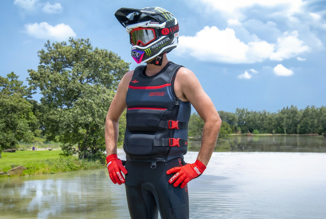 Person wearing a life jacket and helmet by a lake with trees in the background. #color_red