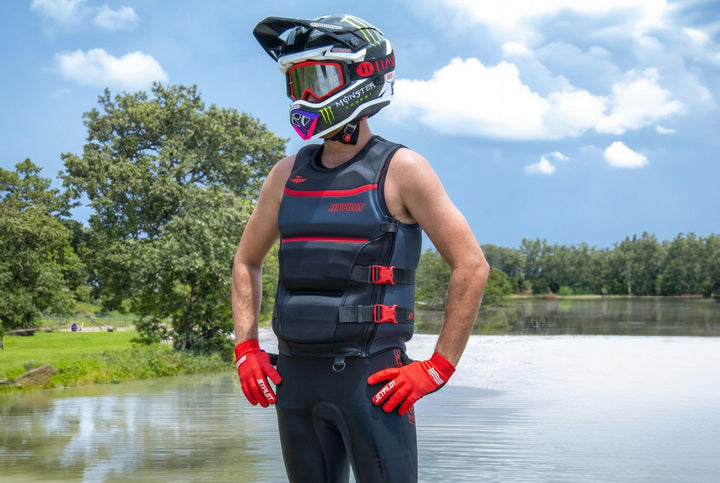 Person wearing a life jacket and helmet by a lake with trees in the background. #color_red