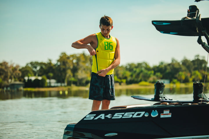 Person in a yellow life jacket standing on a boat with a clear sky and water background. #color_yelbrz