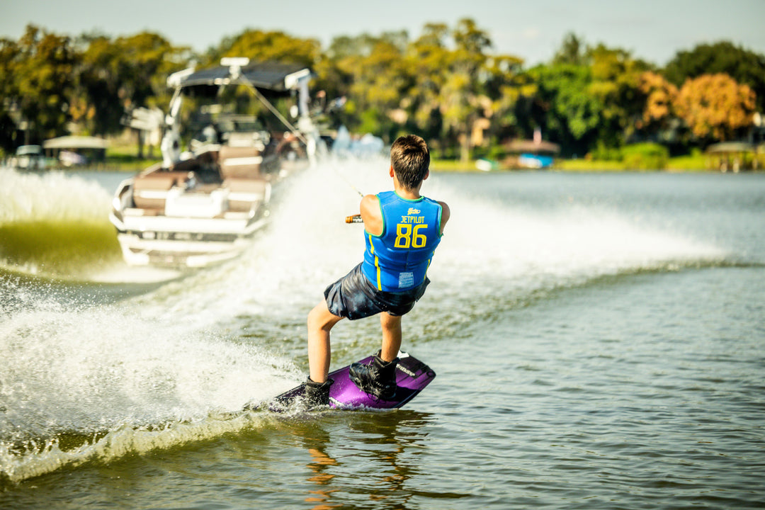 Person wakeboarding behind a boat on a lake with trees in the background. #color_yelbrz