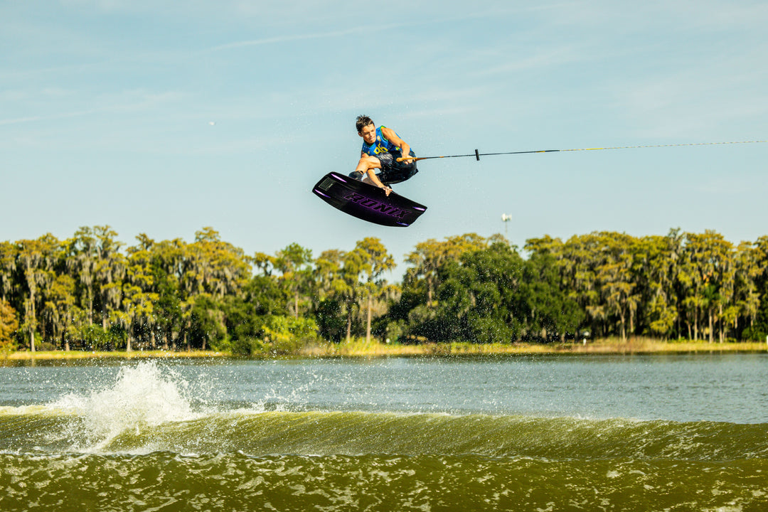 Person wakeboarding in mid-air over a body of water with trees in the background. #color_yelbrz