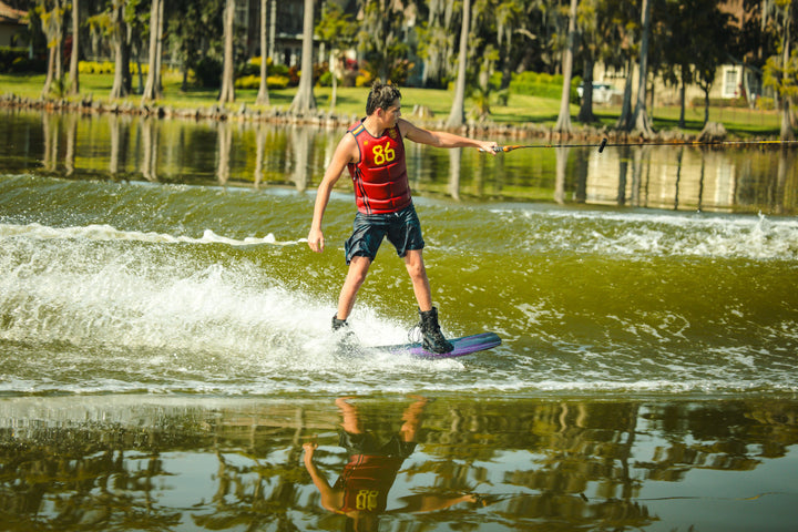 Person wakeboarding on a lake with trees and greenery in the background. #color_redspn
