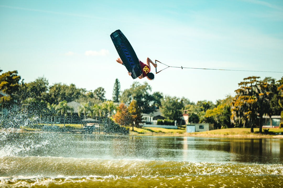 Person wakeboarding on a lake with trees and houses in the background. #color_redspn