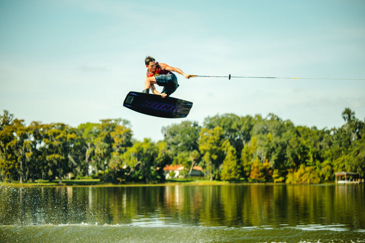 Person wakeboarding on a lake with trees in the background. #color_redspn