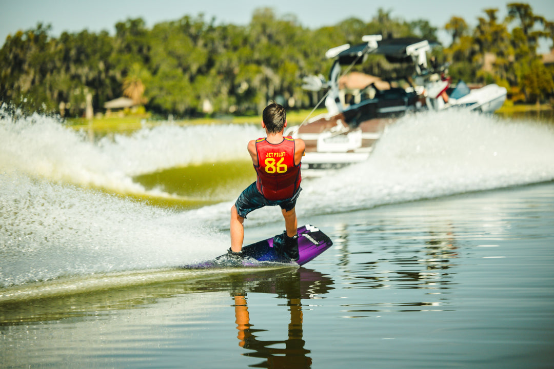 Person wakeboarding on a lake with a boat in the background. #color_redspn