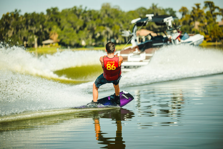 Person wakeboarding on a lake with a boat in the background. #color_redspn