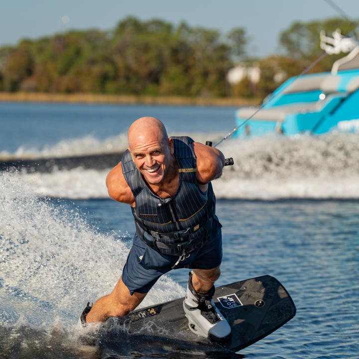 Man wakeboarding on a lake with trees and a boat in the background. #color_gray