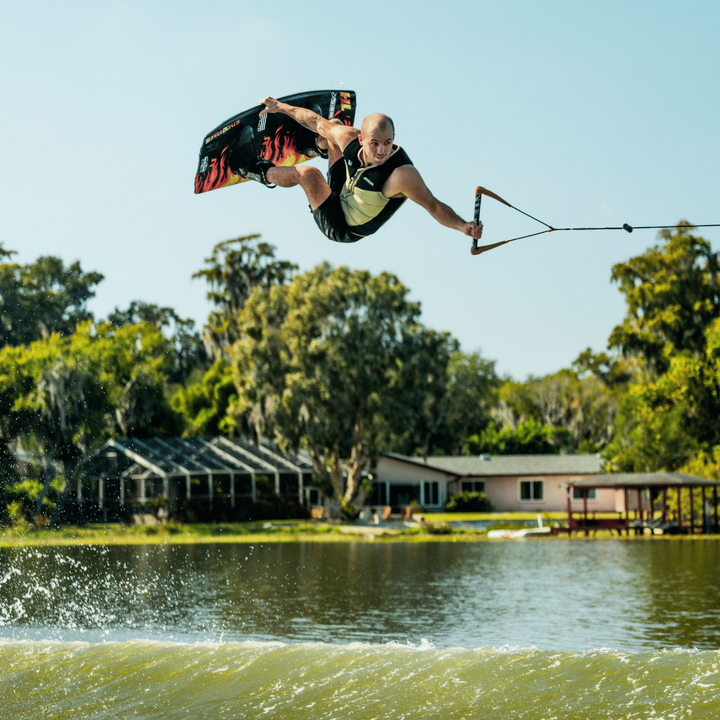 Person wakeboarding on a lake with houses and trees in the background. #color_khaki