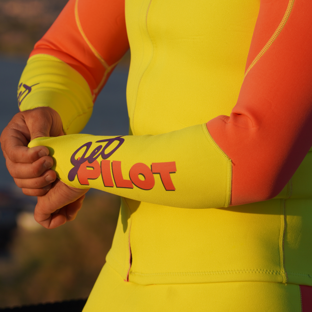 Person wearing a bright yellow and pink Jetpilot wetsuit with a blurred background. #color_neon-pink